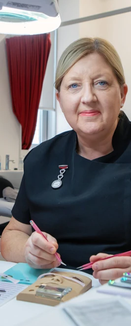 A beauty therapy student applies eyelash extensions to a mannequin head under a magnifying lamp in a professional training environment. A beauty therapy student applies eyelash extensions to a mannequin head under a magnifying lamp in a professional training environment.